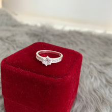 Load image into Gallery viewer, A silver engagement ring with a central zirconium diamond surrounded by smaller clear crystals on a white band.
